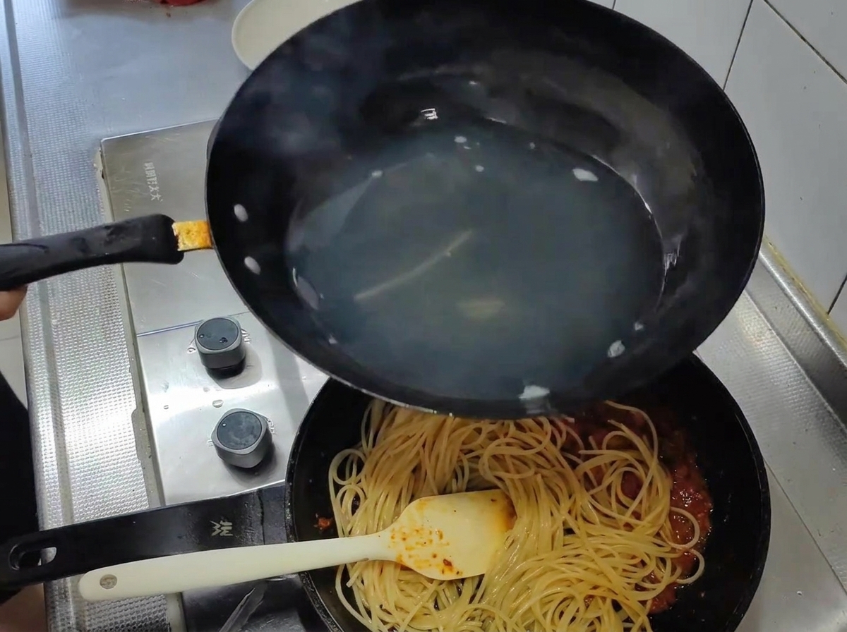 Ugotowane spaghetti przekładane z wody bezpośrednio na patelnię z sosem pomidorowym.