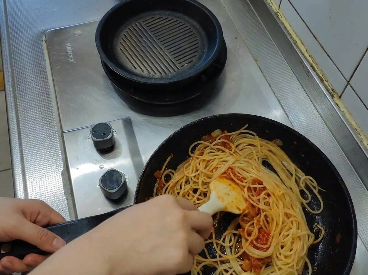 Chochla wlewa mętną, wrzącą wodę z makaronu na patelnię ze spaghetti i sosem.