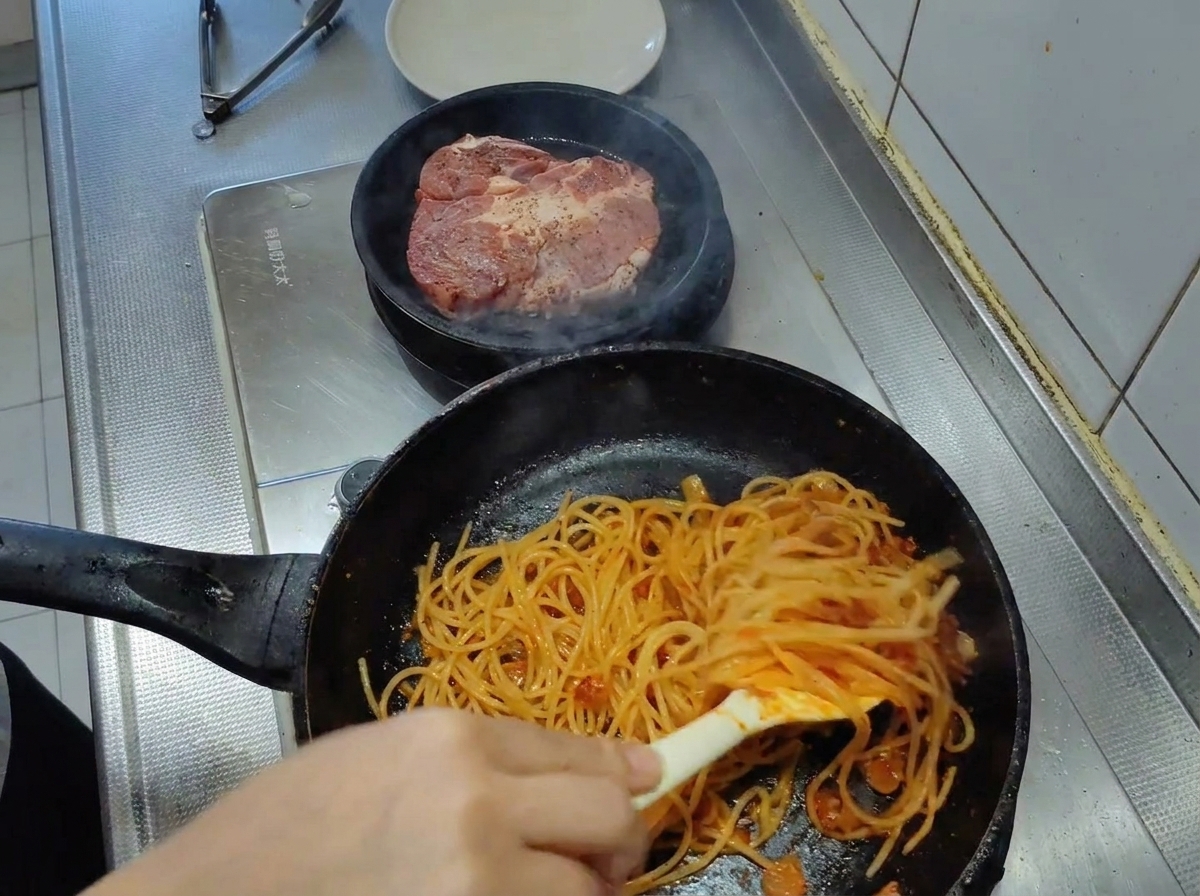 Spaghetti mieszane szczypcami na patelni, dokładnie pokryte gęstym sosem pomidorowym.