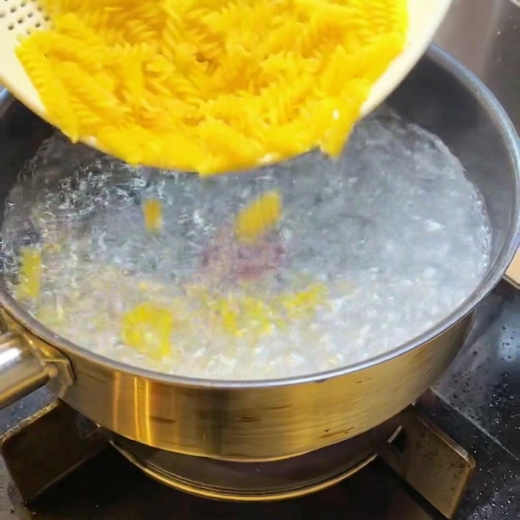 Surowy makaron fusilli wrzucany do garnka z wrzącą wodą.