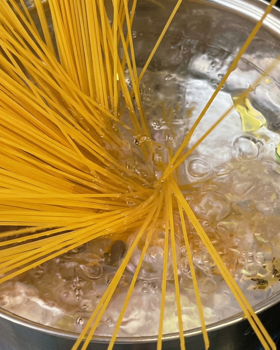 Makaron al dente wyjmowany z garnka za pomocą szczypiec, nad garnkiem unosi się para.