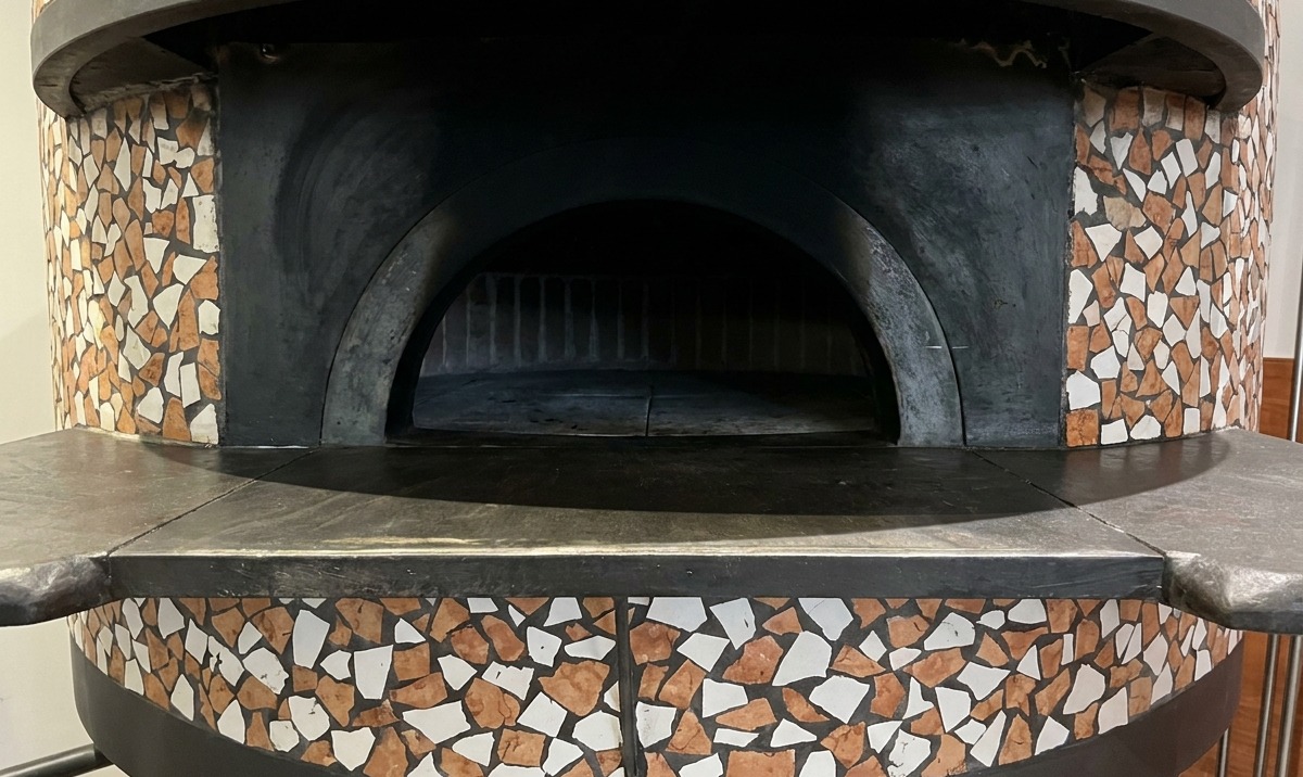 Pizza piekąca się w piecu ceglanym, z brzegami nabierającymi rumianych kolorów.