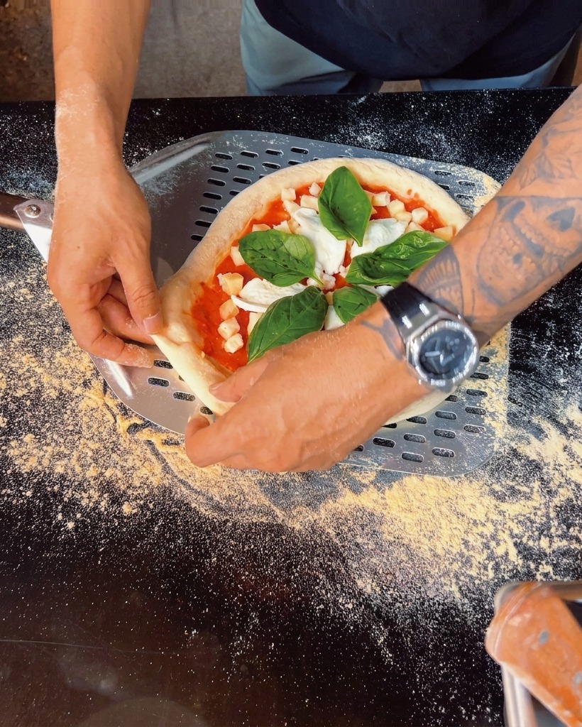 Zbliżenie na listki świeżej bazylii kładzione na pizzy.