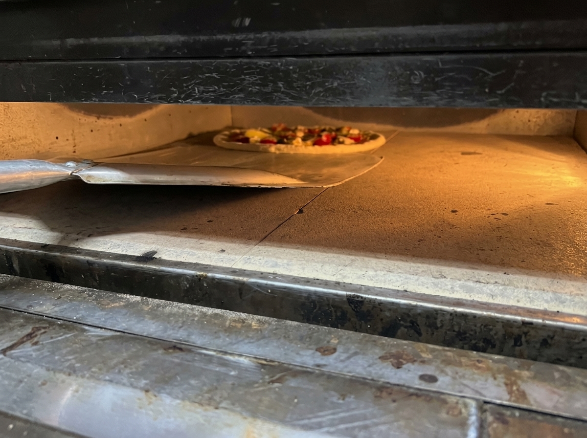 Zsuwanie przygotowanej pizzy z metalowej łopaty do gorącego piekarnika na kamień do pieczenia.