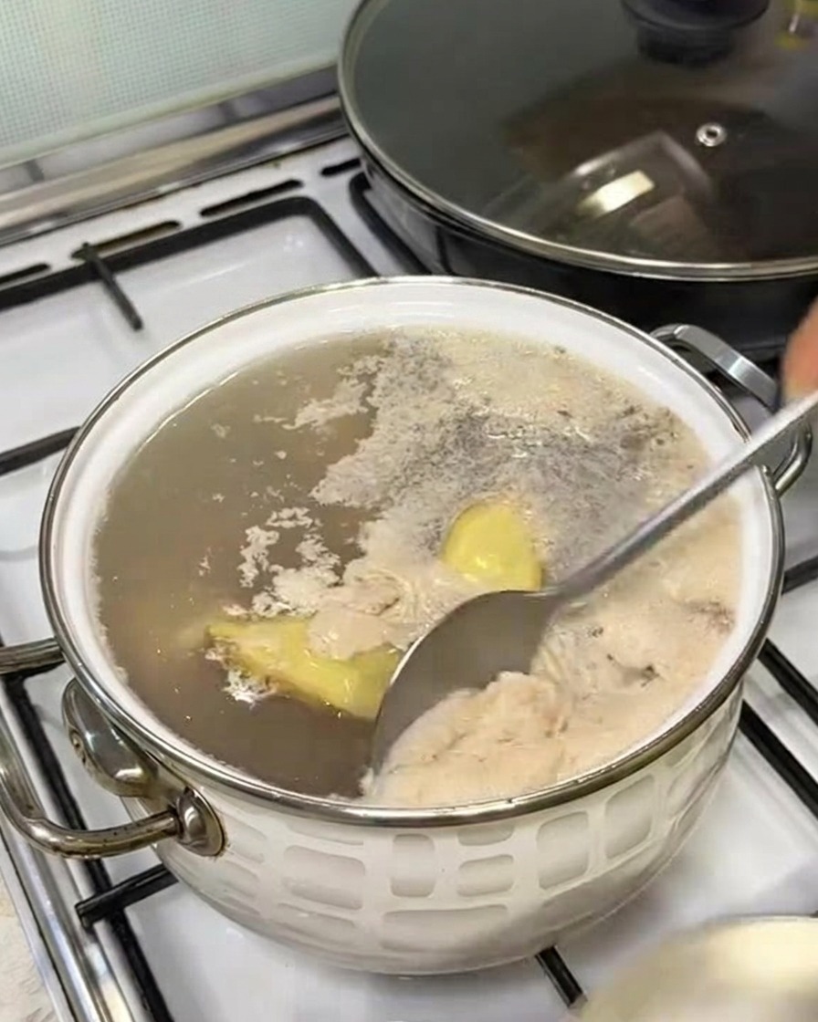 Łyżka zbierająca szarą pianę z powierzchni gotującej się wody.