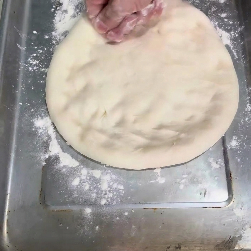 Ciasto spłaszczane na okrągły kształt na blaszce do pieczenia.