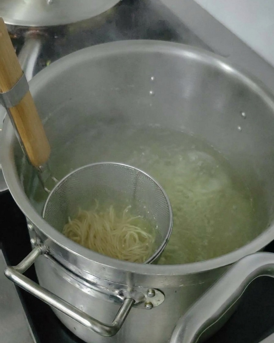Ugotowany makaron ramen wyjmowany z wody w sitku przed dodaniem do miski.