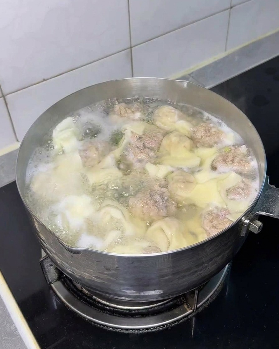 Kwadratowy blok suchego makaronu instant zanurzany w garnku z pierożkami i pulpecikami.