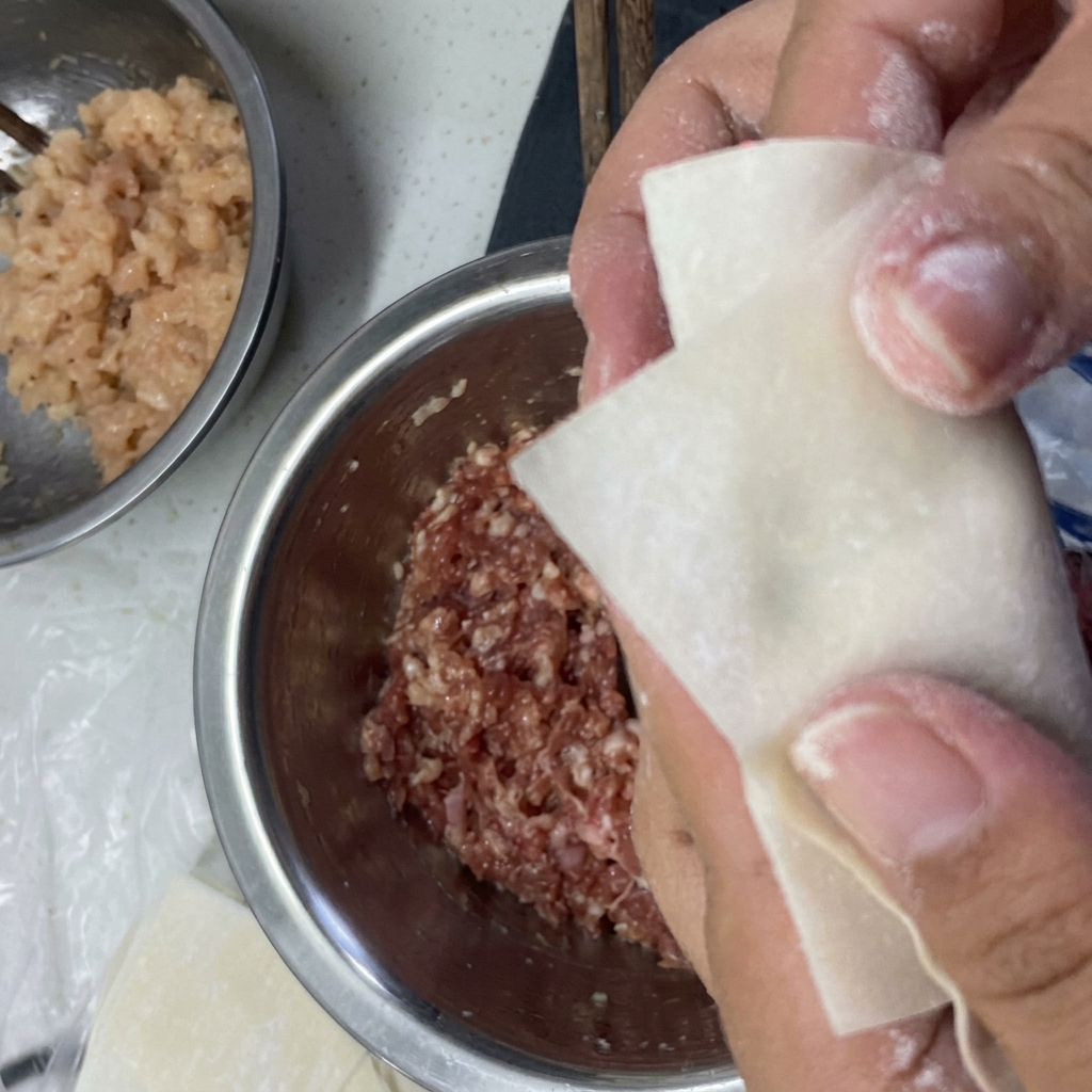 Ręce składające ciasto wonton wokół nadzienia i uszczelniające brzegi za pomocą wody.
