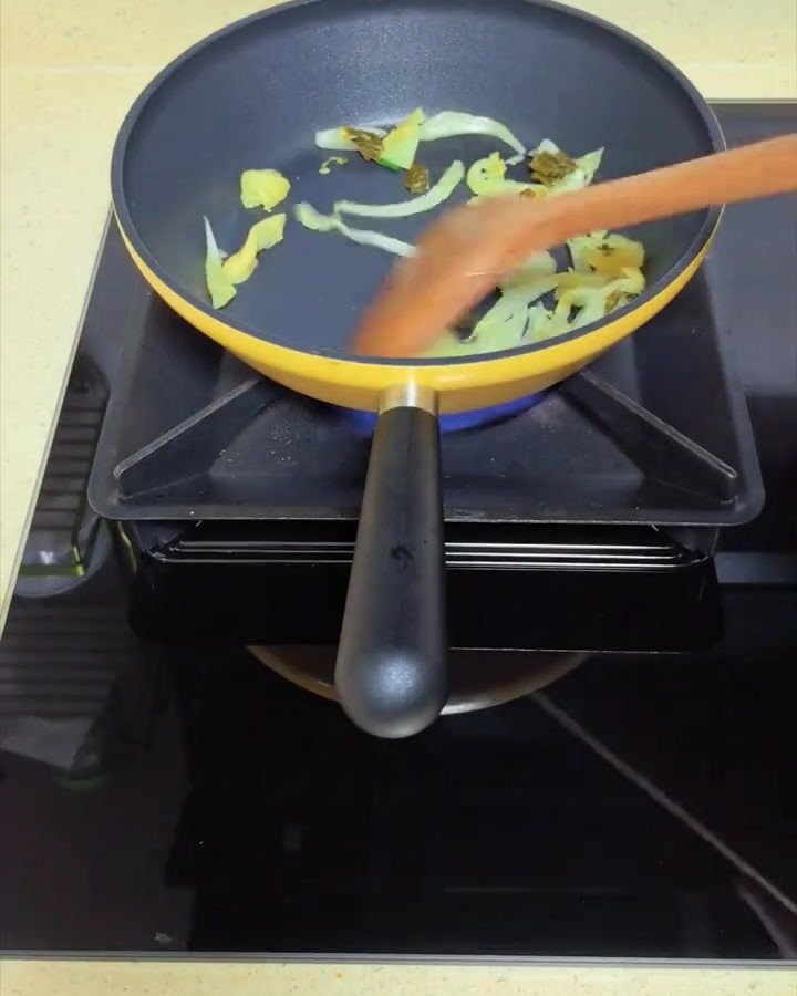 Kiszona kapusta musztardowa podsmażana na żółtej patelni za pomocą drewnianej łopatki.