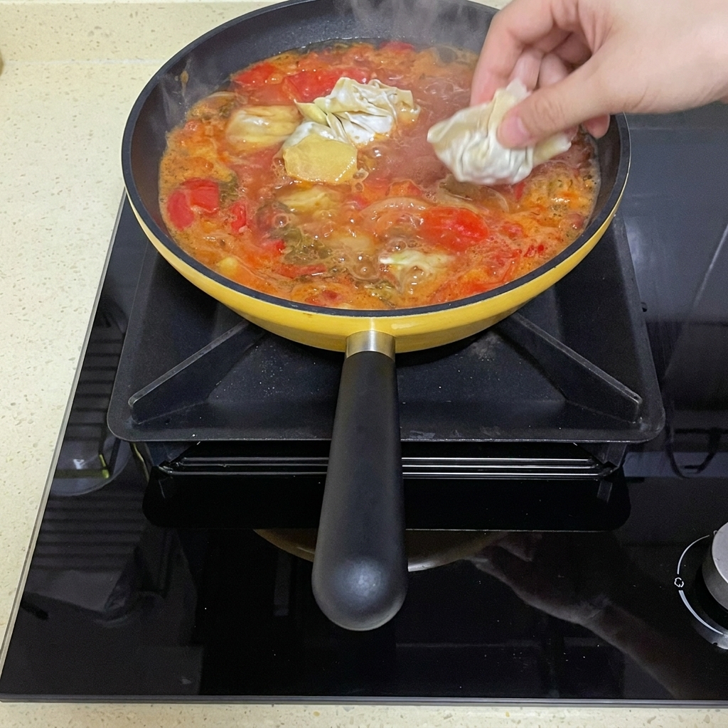 Surowe pierożki wonton wrzucane do wolno gotującego się pomidorowego bulionu.