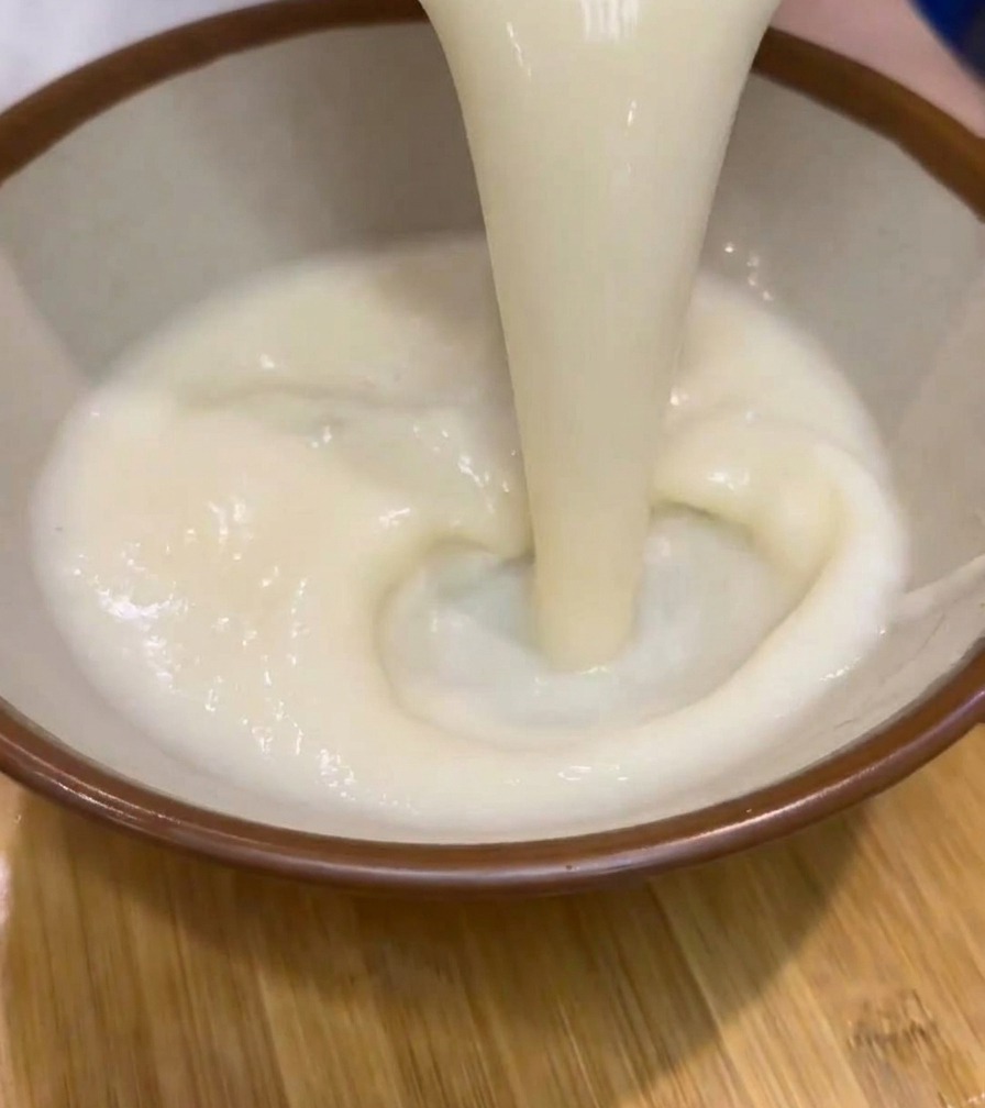 Gęsta, kremowa biała zupa ramen wlewana z dzbanka do ceramicznej miski.
