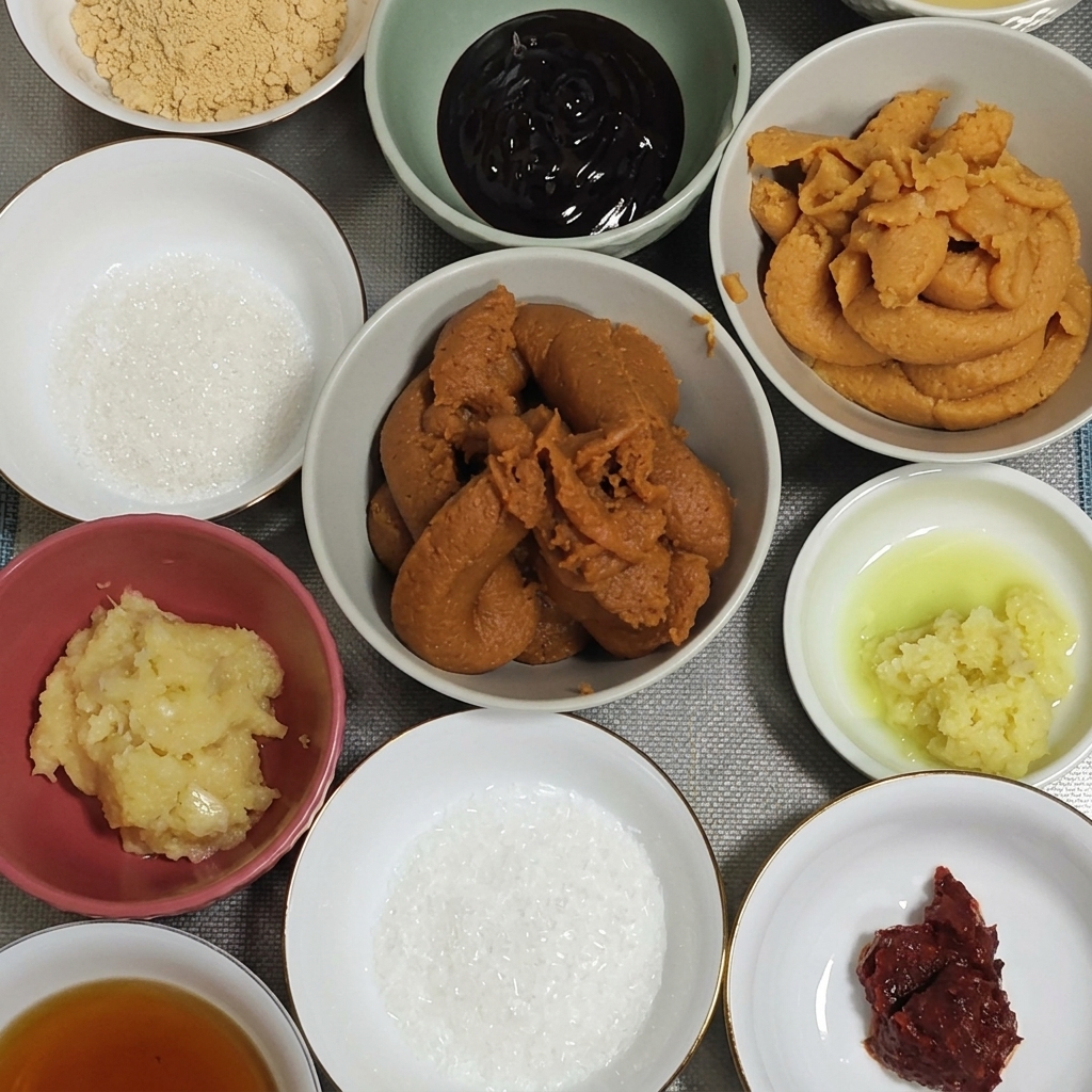 Duża łyżka gęstej, ciemnoczerwonej pasty miso wkładana do miski z czosnkiem i imbirem.