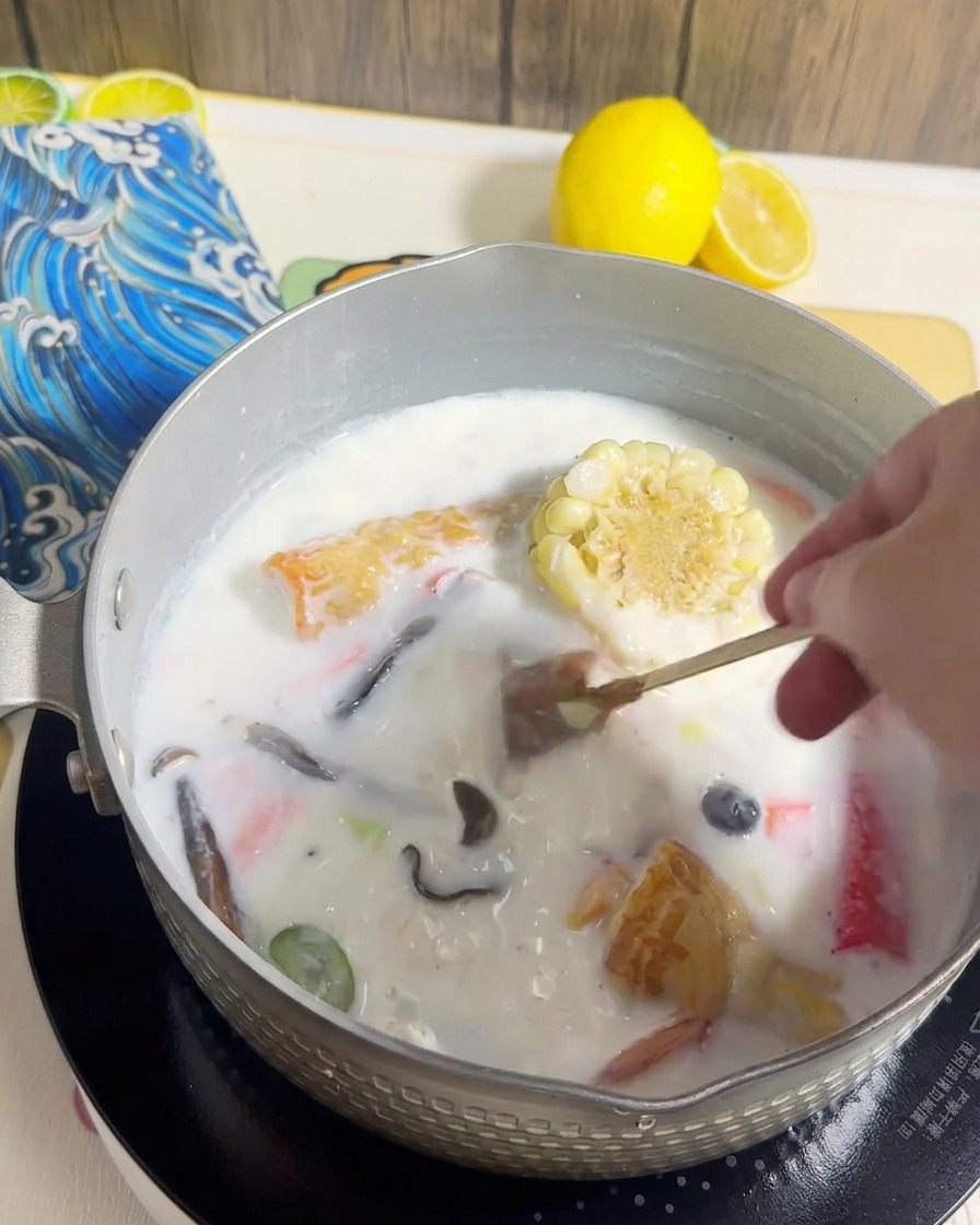 Makaron ramen dodawany do garnka z kremowym bulionem i ugotowanymi dodatkami.