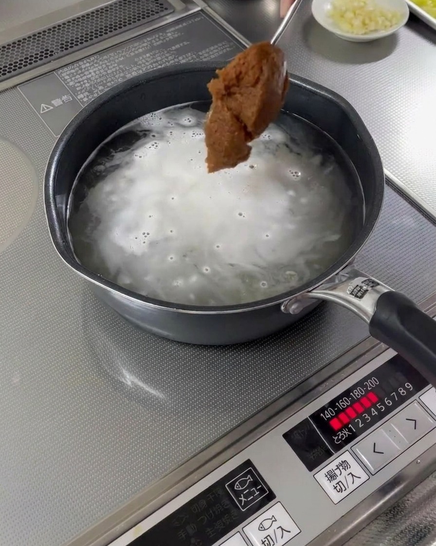 Łyżka pasty miso dodawana do garnka z gotującym się bulionem.