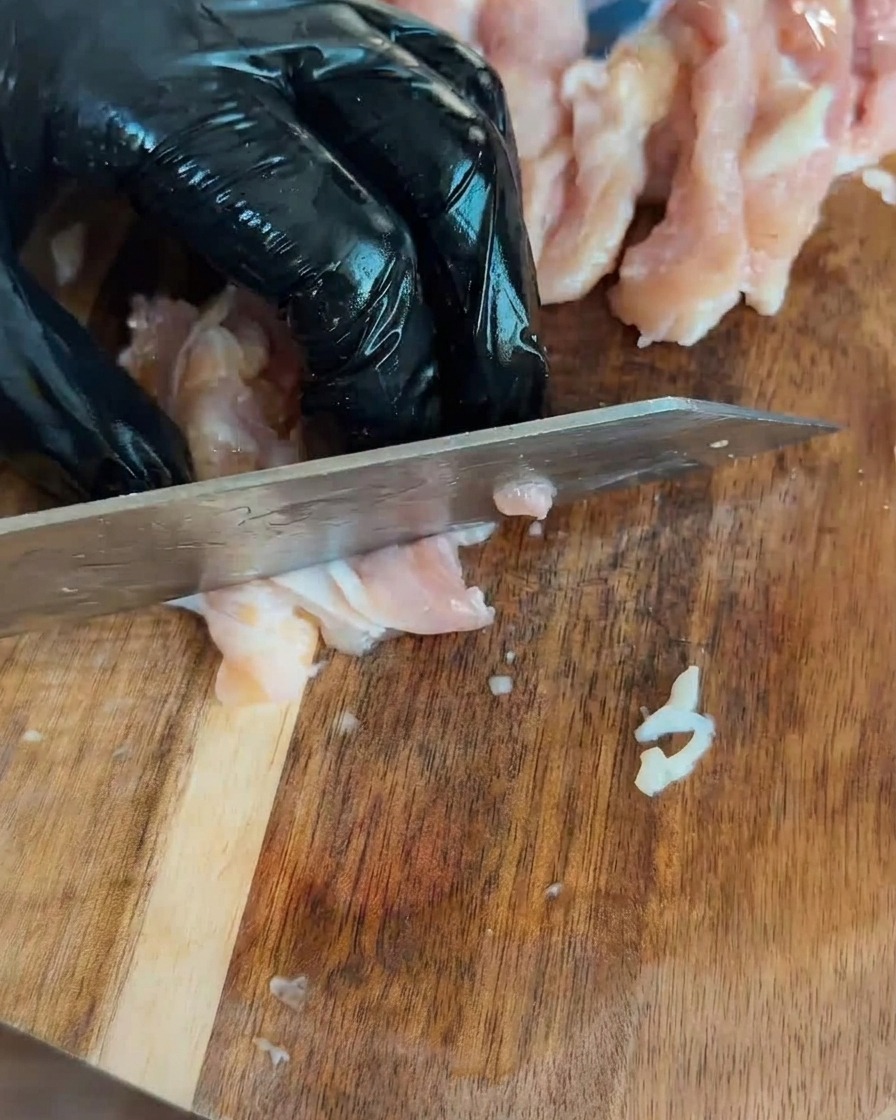 Kawałki surowego kurczaka pokrojone w kostkę na drewnianej desce.