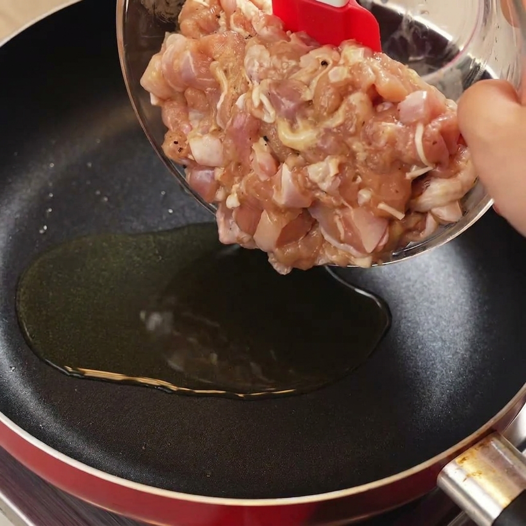 Przekładanie surowego kurczaka w marynacie za pomocą czerwonej szpatułki na gorącą patelnię.