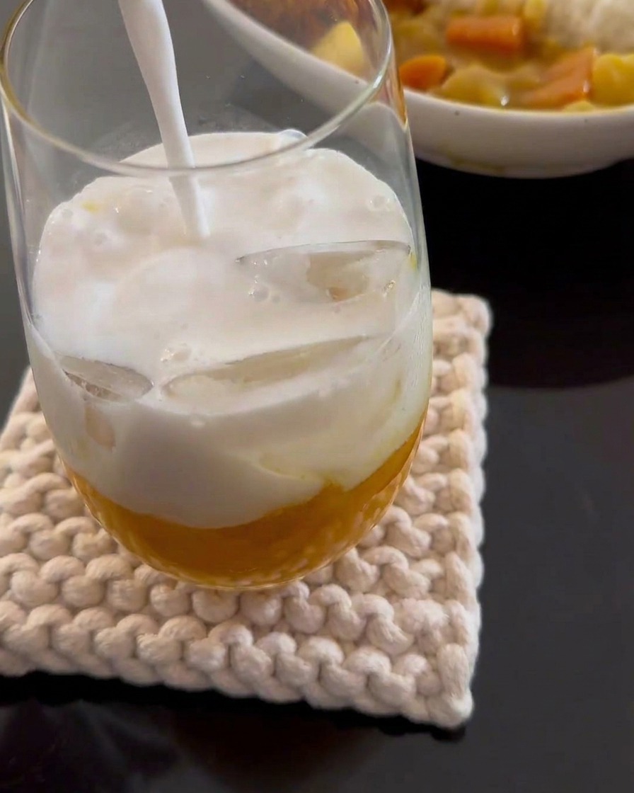 Białe mleczko kokosowe wlewane do wysokiej szklanki zawierającej żółte puree z mango i kostki lodu.