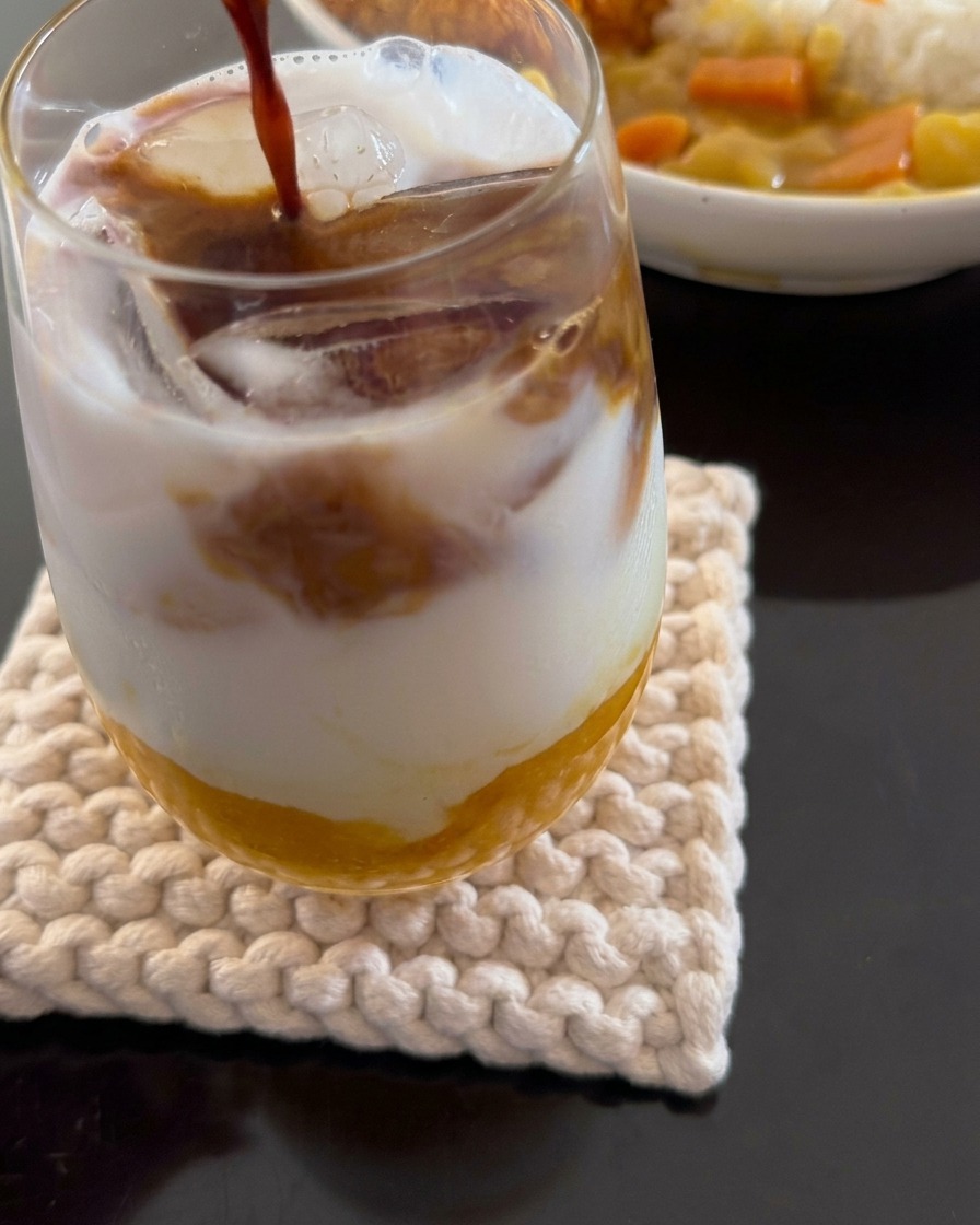 Zbliżenie pokazujące espresso nalewane do warstwowego napoju z pulpy mango, mleczka kokosowego i lodu.