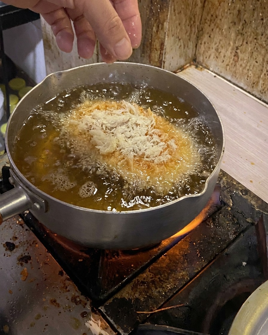 Panierowany kotlet wieprzowy wkładany do garnka z gorącym olejem.