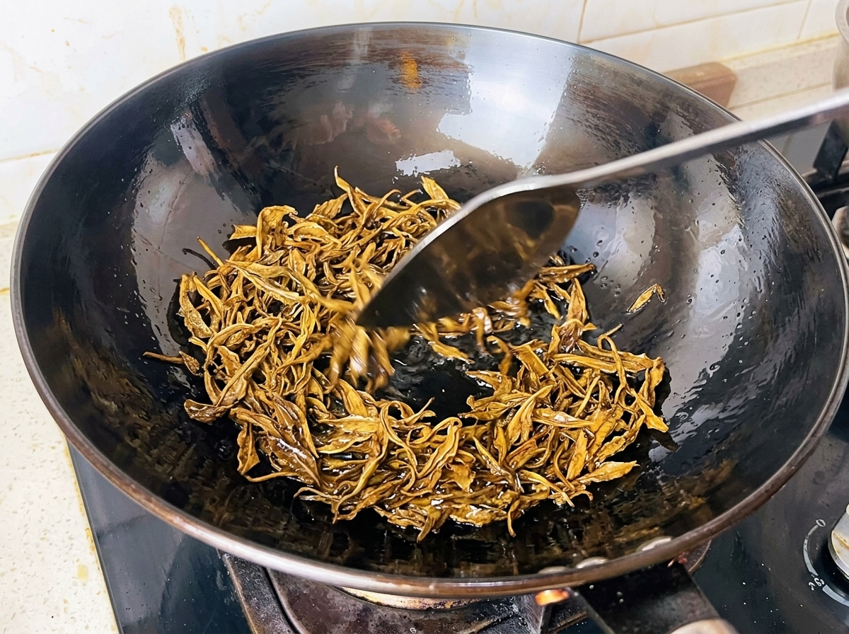 Wilgotne liście zielonej herbaty smażone na gorącym oleju w czarnym woku za pomocą metalowej łopatki.