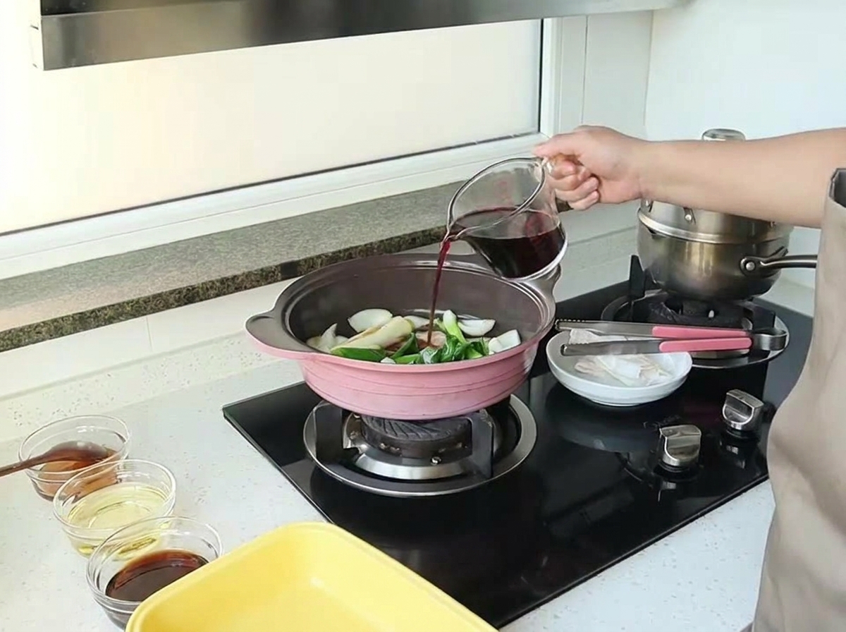 Ręka wlewa czerwone wino z miarki do patelni z podsmażonymi aromatami.