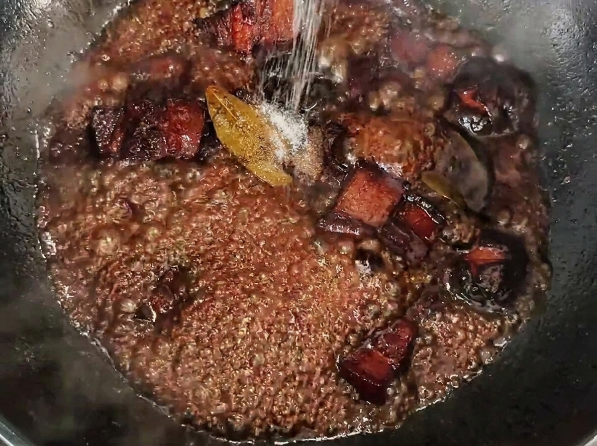 Sól posypywana na duszące się kostki boczku w ciemnym, gęstym sosie.