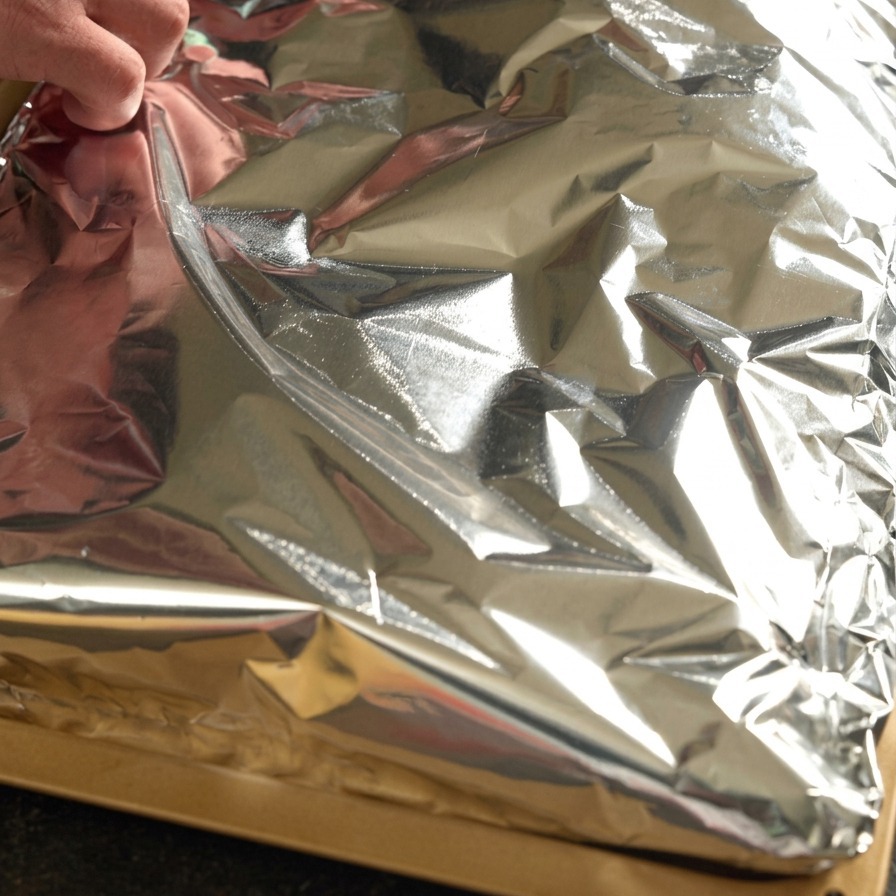 Dłonie szczelnie zawijające płat przyprawionych żeberek w folię aluminiową.