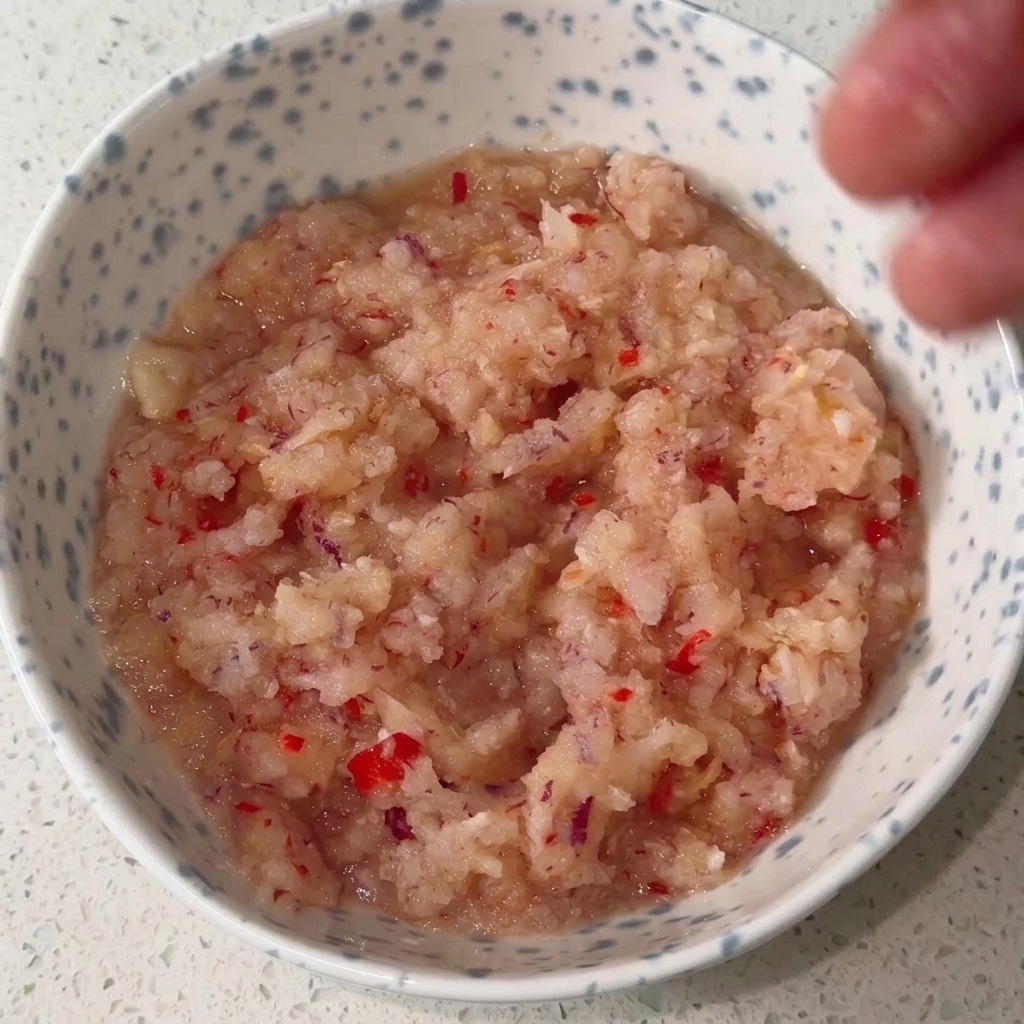 Miska zawierająca zblendowaną bazę z cebuli i chili, mieszaną z różnymi płynnymi i sypkimi przyprawami, tworząca gęsty, czerwony sos.