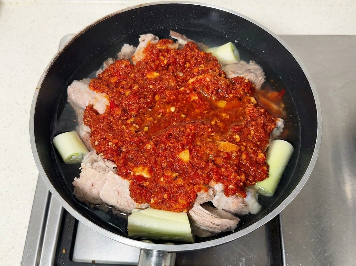 Żeberka wieprzowe pokryte czerwoną pastą chili na patelni wypełnionej wodą.