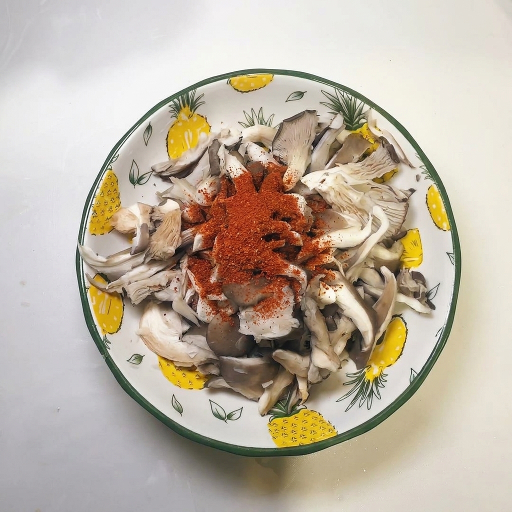 Kopczyk czerwonej przyprawy chili na wierzchu odciśniętych pasków boczniaków w misce.