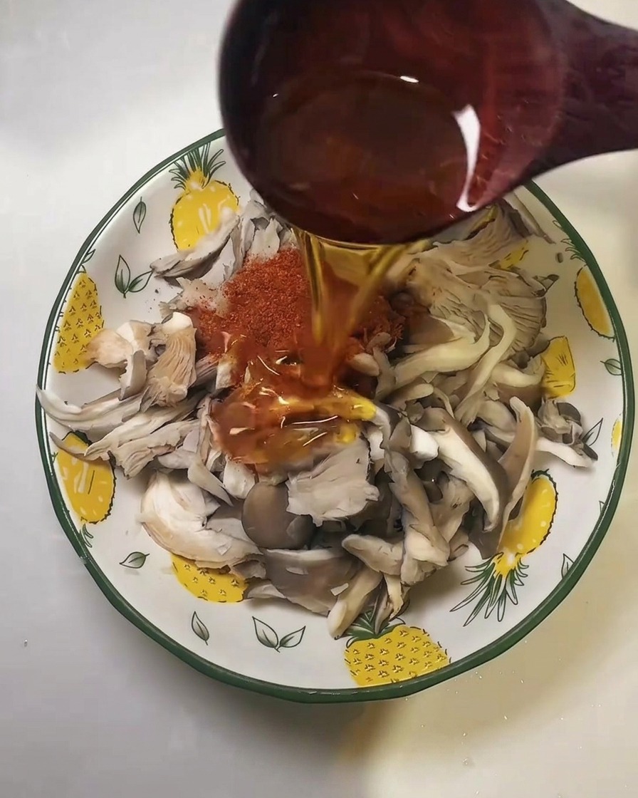 Olej wlewany z drewnianej łyżki na przyprawę chili i boczniaki.