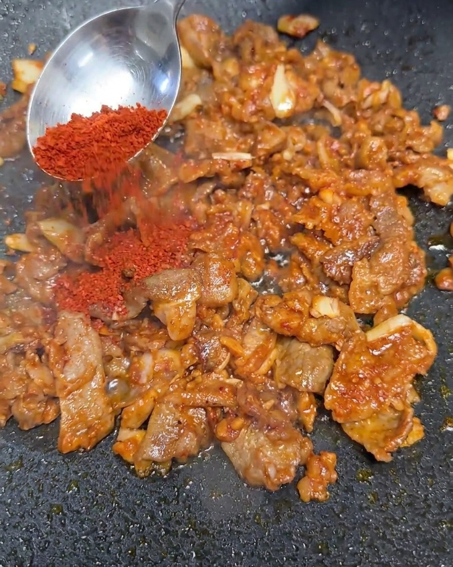 Czerwone płatki chili dodawane do podsmażonej mieszanki wołowej.