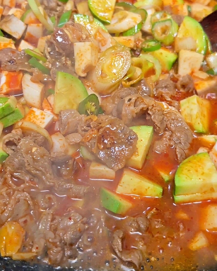 Zbliżenie intensywnie bulgoczącego koreańskiego gulaszu z kawałkami tofu, wołowiny i zielonej cukinii w czerwonobrązowym bulionie.