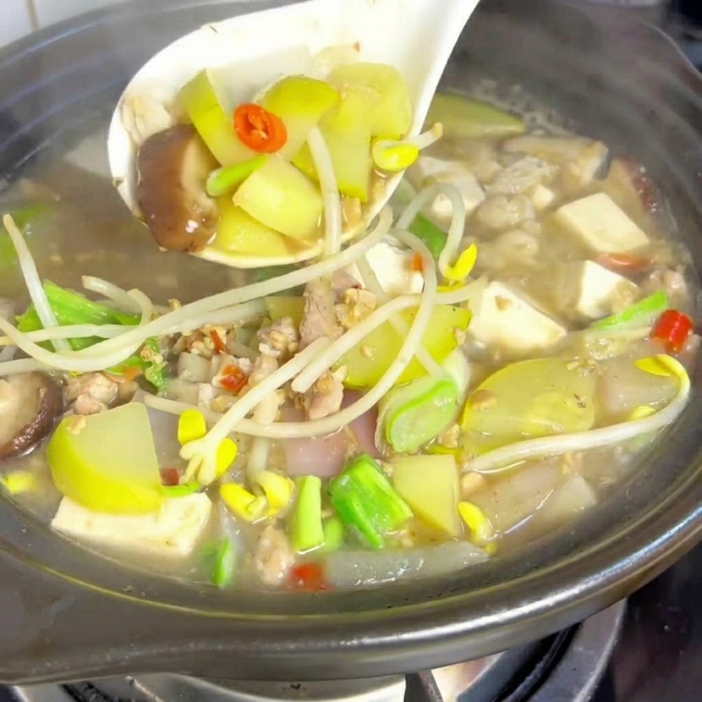 Kostki miękkiego tofu umieszczane w garnku z gotującą się zupą.