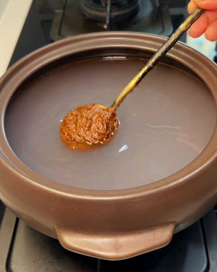 Łyżka brązowej koreańskiej pasty sojowej zanurzana w czystej wodzie w kamiennym garnku.