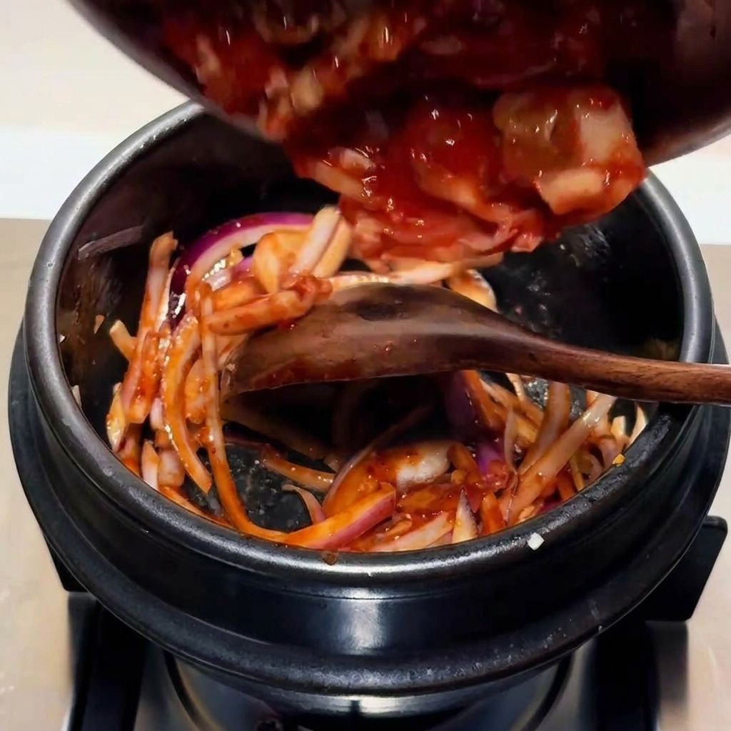 Posiekane kimchi dodawane do garnka z bazą z cebuli i sosu.