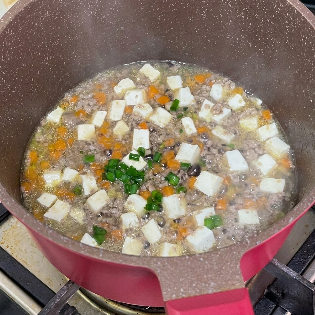 Świeżo posiekany zielony szczypiorek posypywany na gotowy gulasz z wołowiny i tofu na patelni.