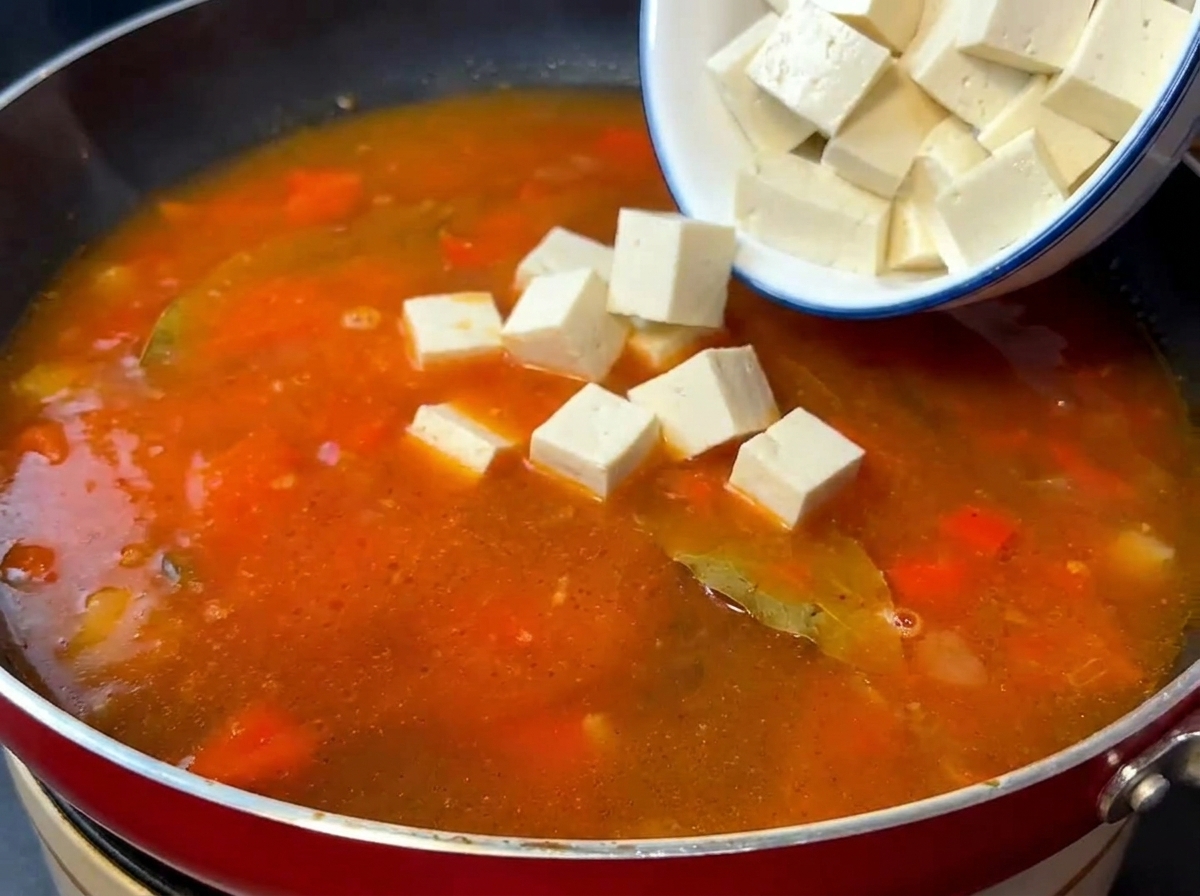 Kostki tofu jedwabistego i podsmażona wołowina dodawane do gotującej się bazy pomidorowej.