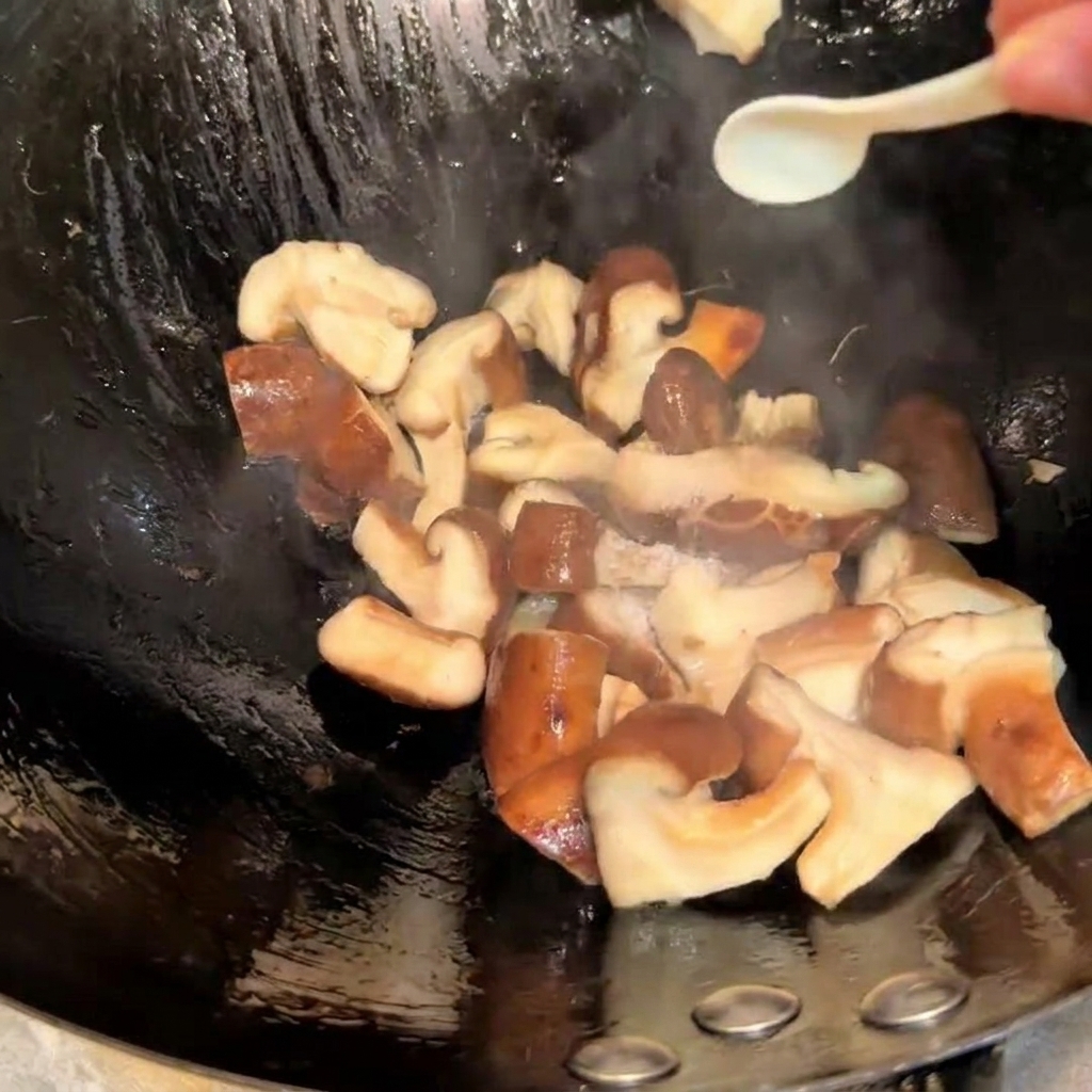 Doprawianie smażących się grzybów shiitake w woku solą i sosem sojowym za pomocą małej łyżeczki.