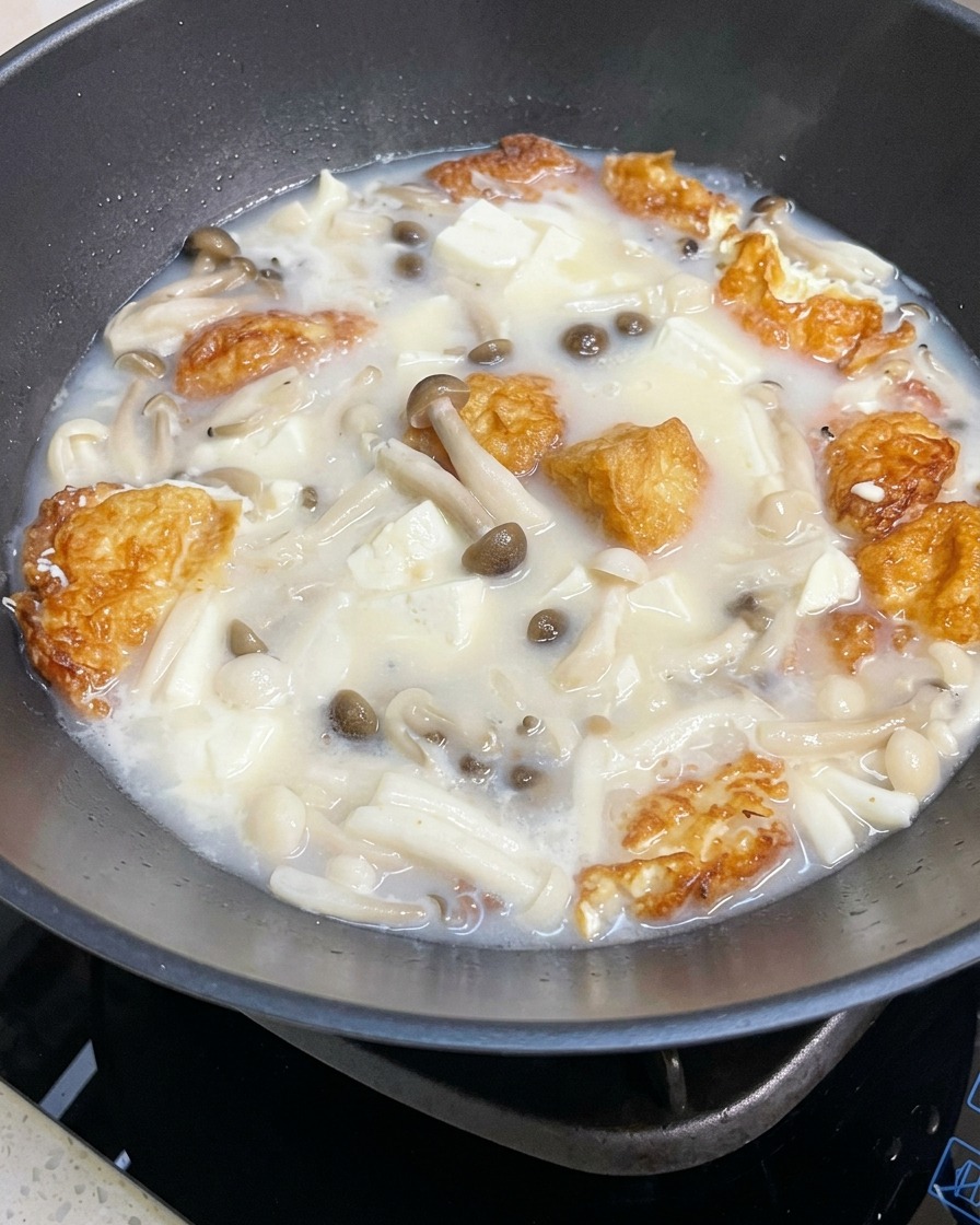 Zbliżenie na gotującą się zupę z grzybami i tofu doprawianą solą i pieprzem.