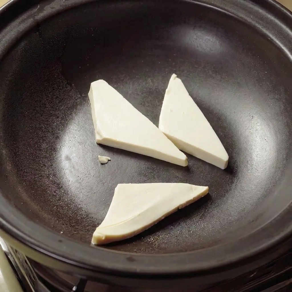 Trójkąty tofu smażące się w gorącym oleju wewnątrz glinianego garnka na złoty kolor.