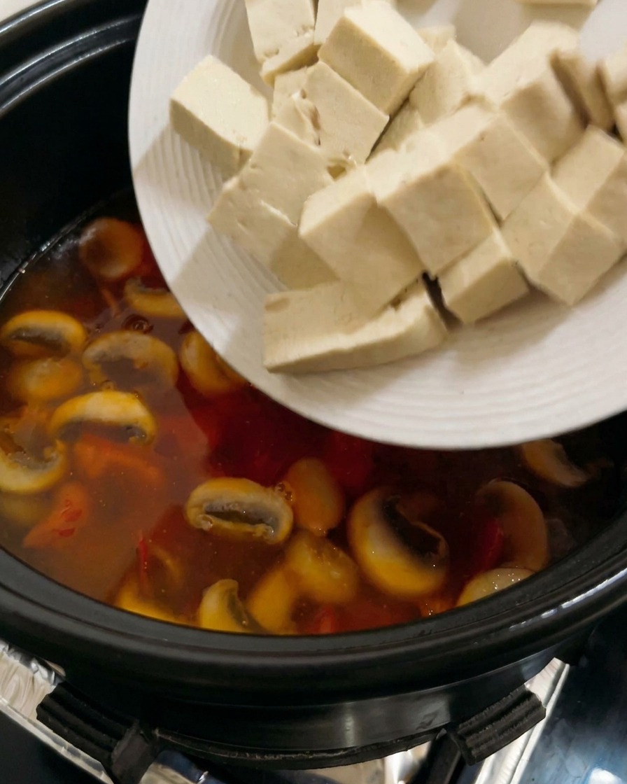 Kostki tofu dodawane do gotującej się zupy pomidorowej z pieczarkami.