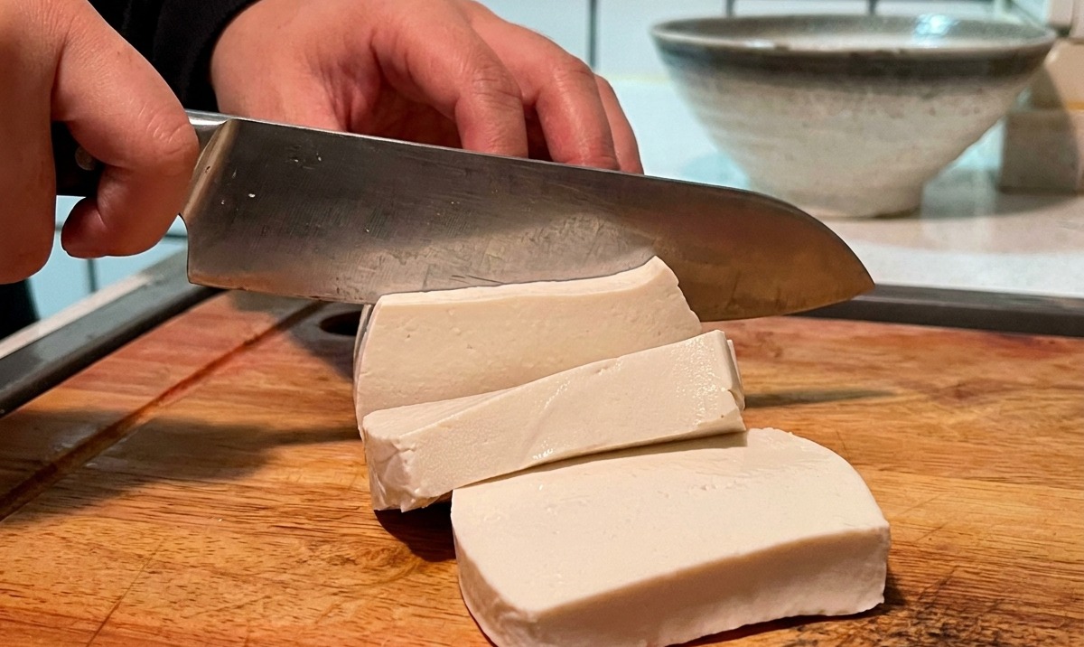 Kostka białego tofu krojona w mniejsze kostki na drewnianej desce.