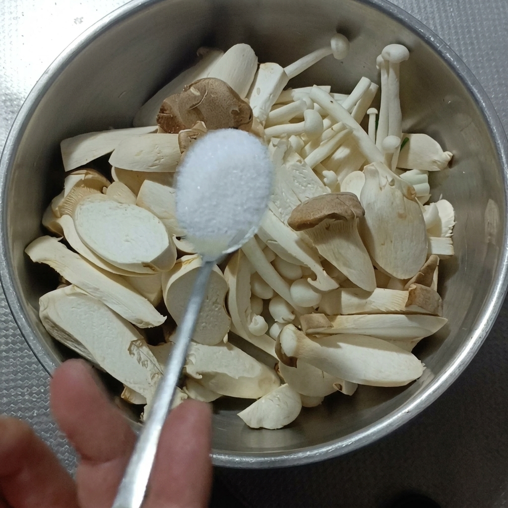 Pokrojone boczniaki i grzyby shimeji w metalowej misce z wodą i solą.