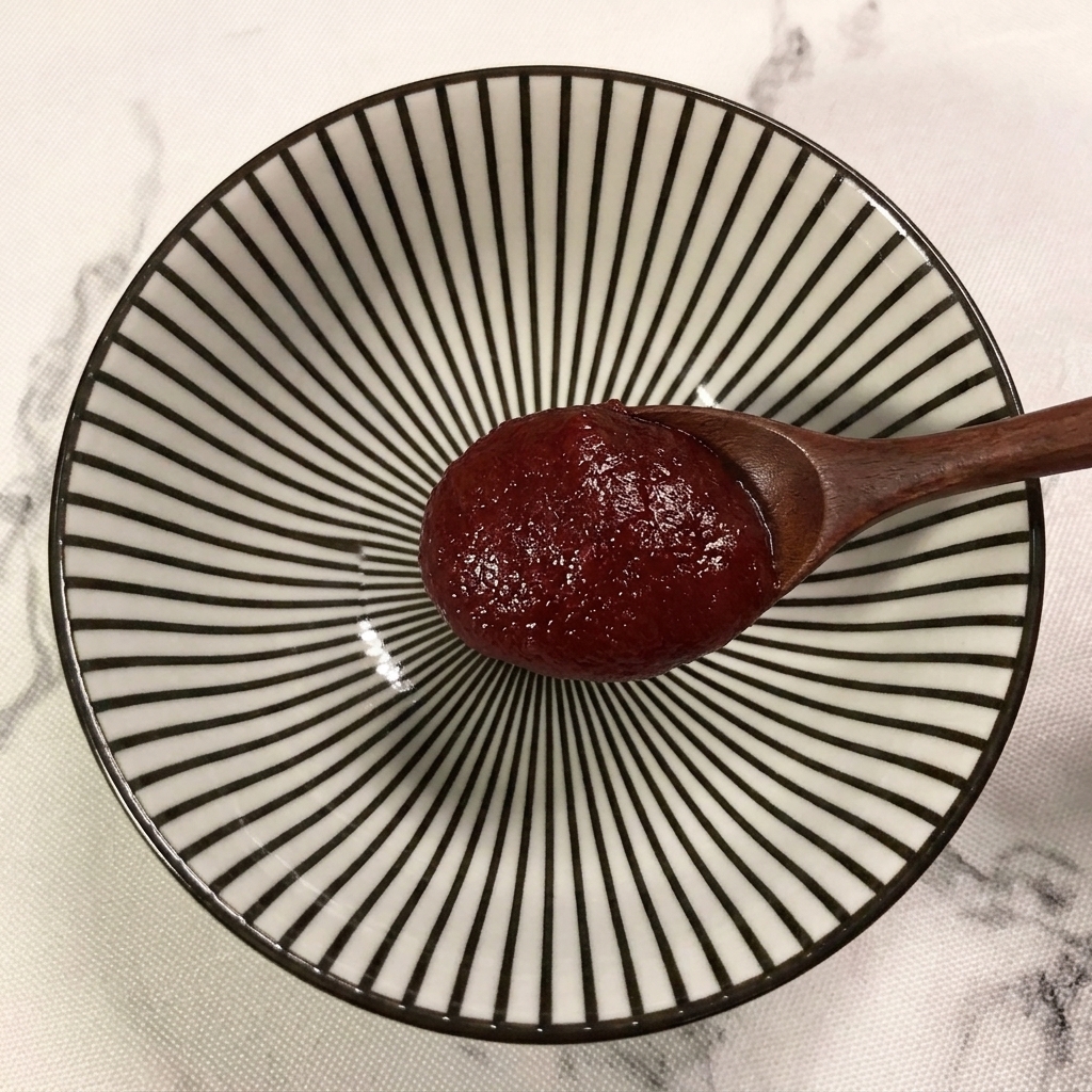 Drewniana łyżka dodająca porcję czerwonej pasty chili do miseczki w paski.