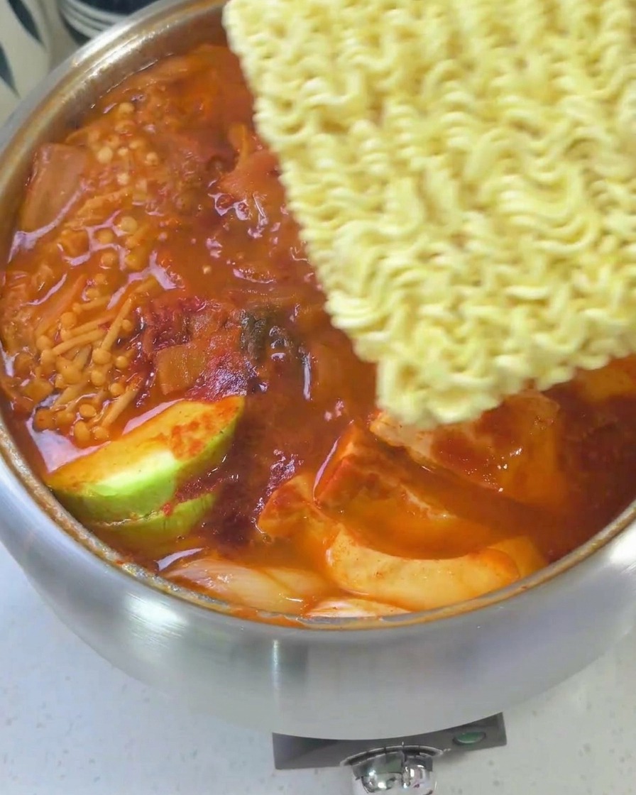 Prawie gotowy gulasz z ułożonym na wierzchu makaronem ramen, żółtym serem i jajkiem.