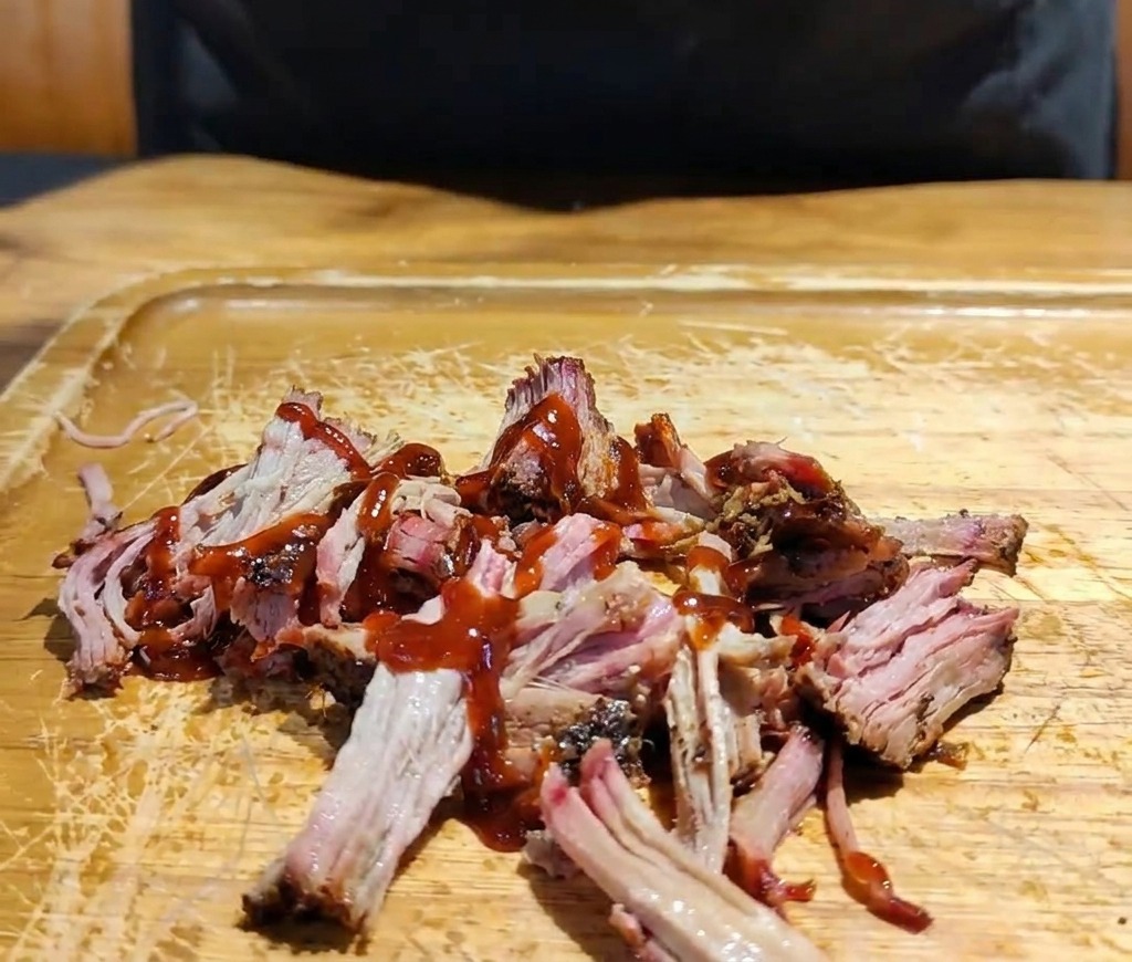 Dłoń nakładająca mieszankę poszatkowanej fioletowej i białej kapusty na porcję mięsa z sosem BBQ.