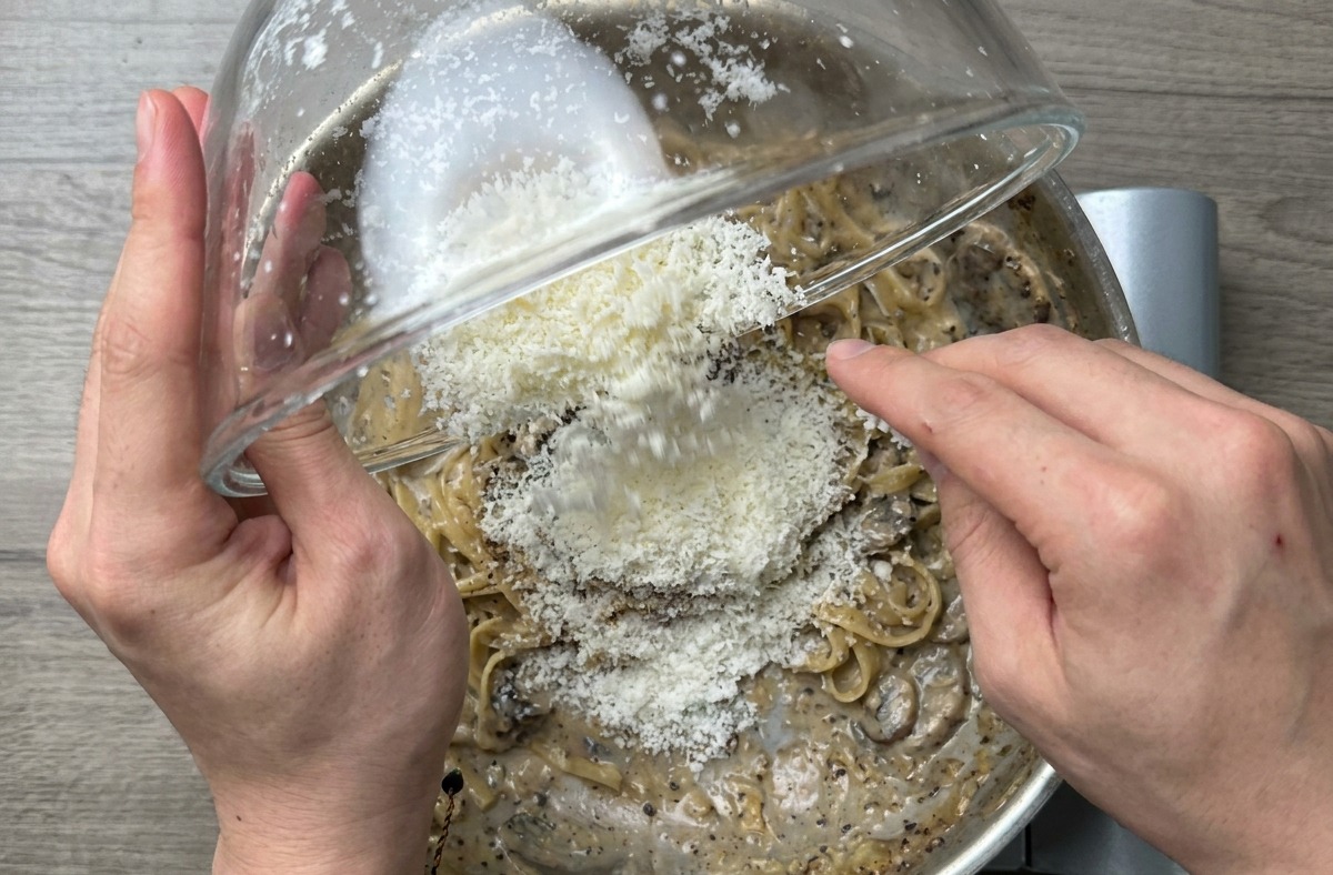 Zbliżenie na gotowe spaghetti mieszane energicznie na patelni dla uzyskania lśniącego, kremowego efektu.