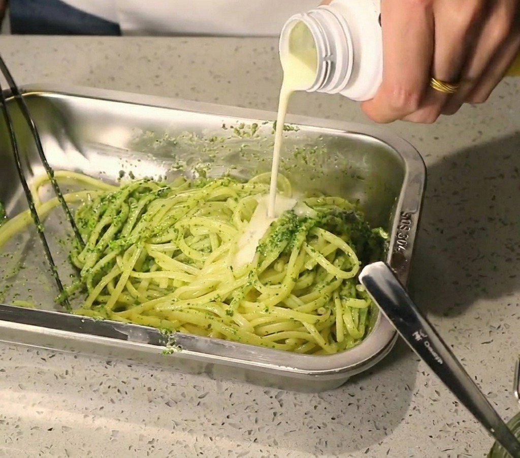 Strumień białego śmietankowego sosu wlewany na makaron z zielonym pesto.